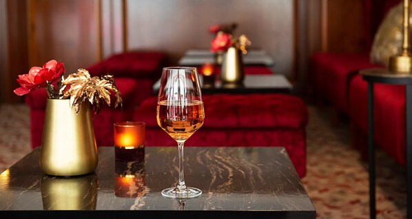 A table with a glass of amber liquid, a gold vase with red flowers, and a candle. - Victor's Residenz-Hotel Leipzig (Leipzig)