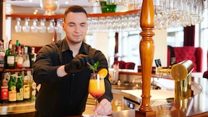 A bartender preparing a drink at a bar with a variety of bottles and glasses in the background. - Victor's Residenz-Hotel Leipzig (Leipzig)