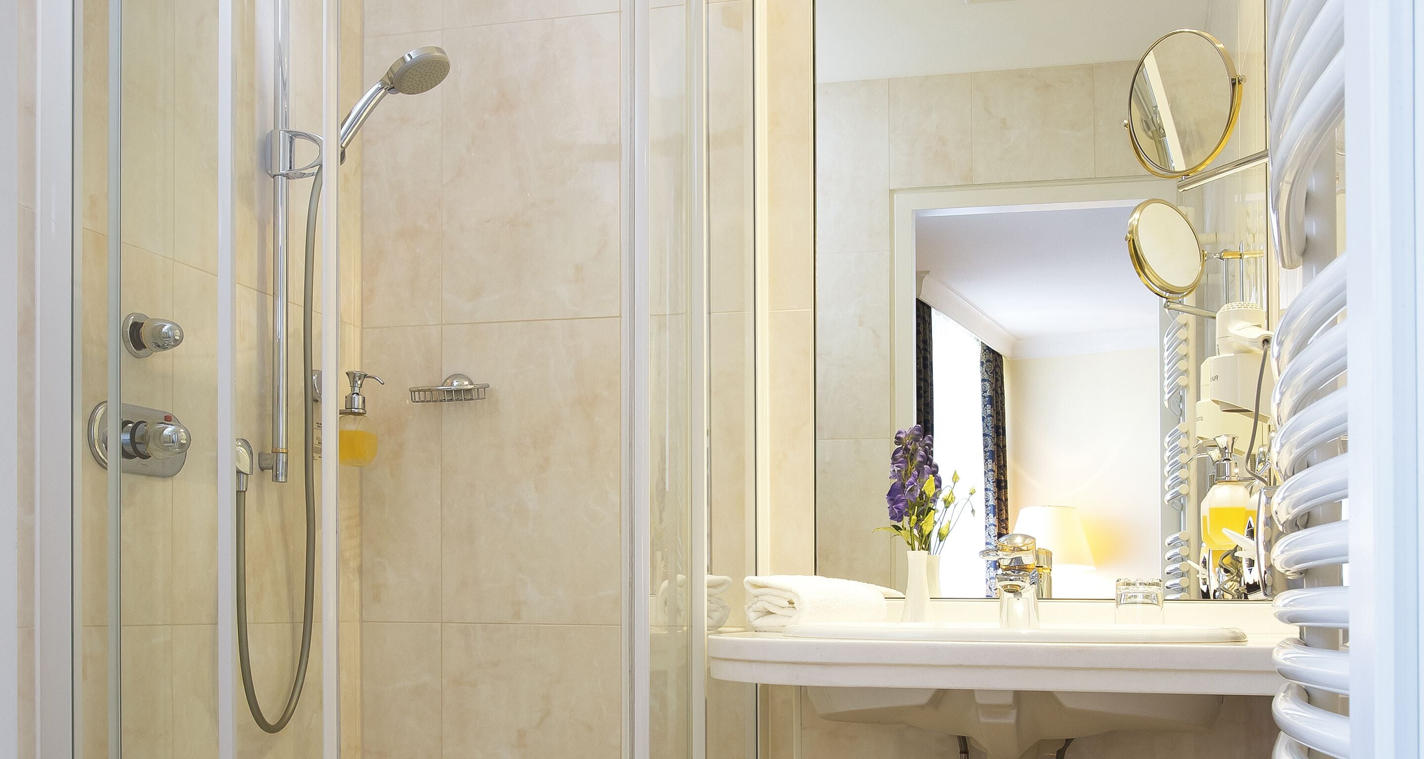 Ein Badezimmer mit einer Duschkabine, einem Waschbecken mit Spiegel und einer Vase mit Blumen.