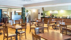 Un restaurant avec des tables et des chaises en bois, un comptoir avec une machine à café et un mur vert orné d’œuvres d’art.