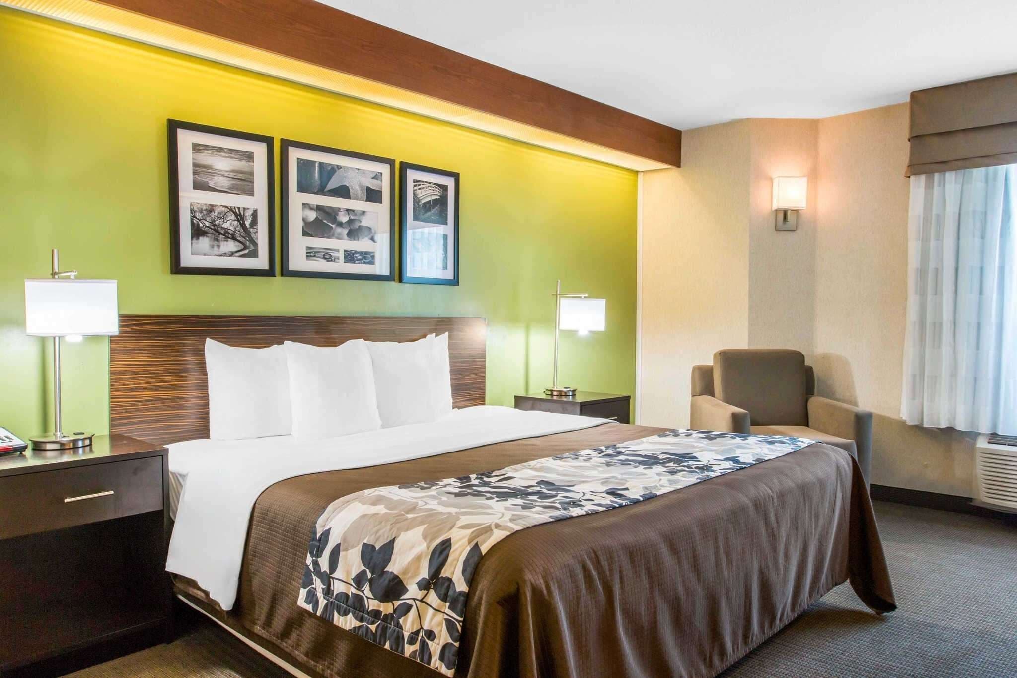 Een hotelkamer met een groot bed, twee bedlampen, een stoel en wanddecoraties in lijsten.