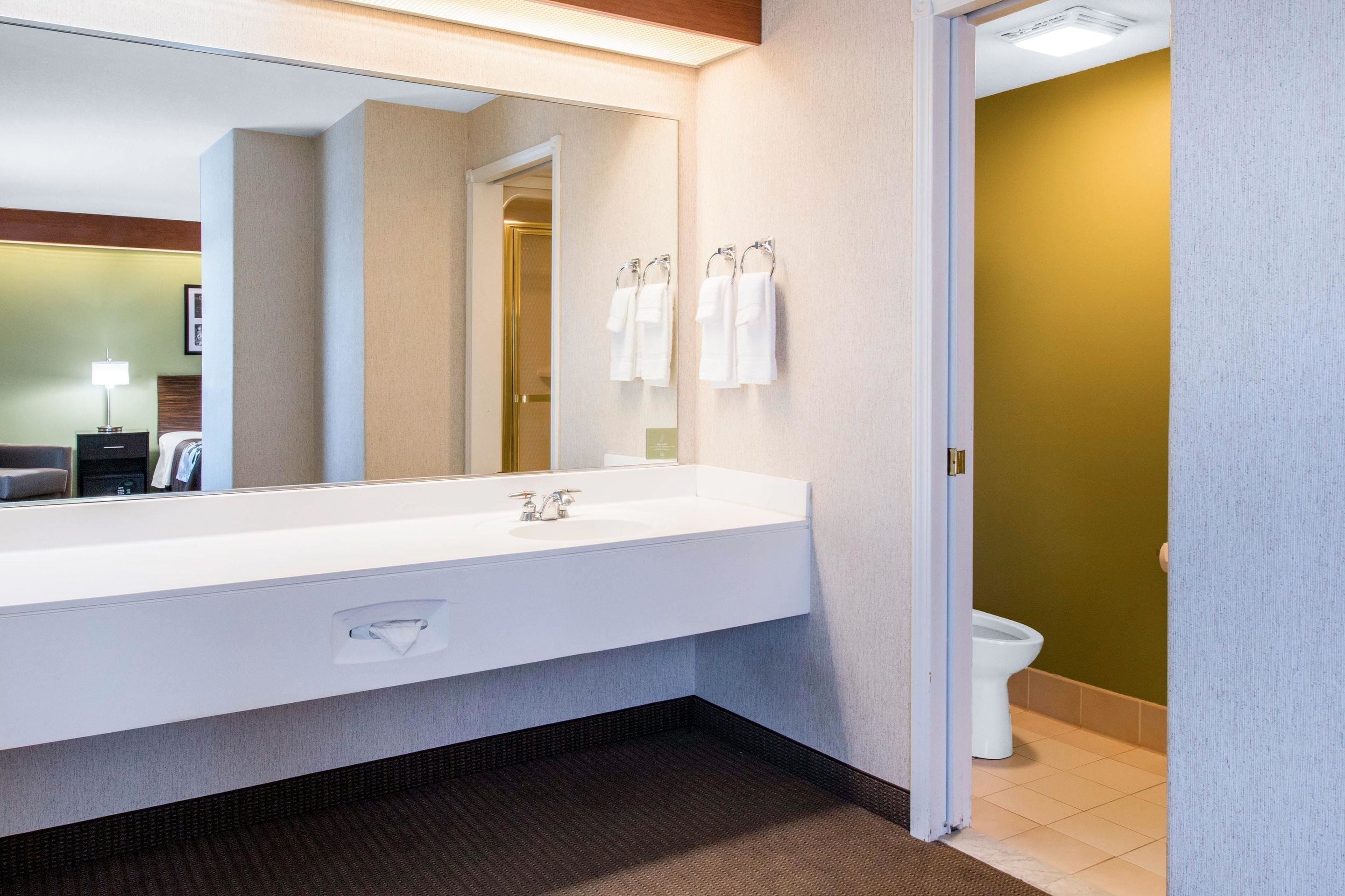 A modern bathroom with a large mirror, white sink, and two towels hanging on hooks.