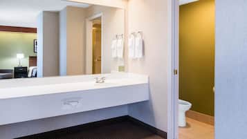 A modern bathroom with a large mirror, white sink, and two towels hanging on hooks.