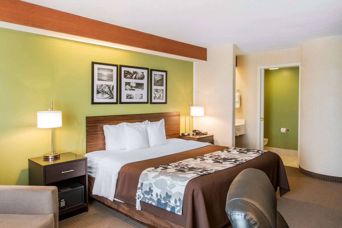 A hotel room with a bed, two bedside tables with lamps, a chair, and framed pictures on the wall.