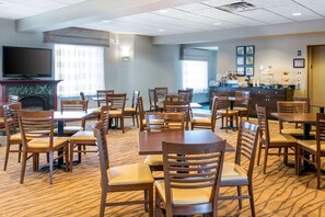 A hotel dining area with multiple tables and chairs, a fireplace, a television, and a kitchen counter with various items. - Sleep Inn & Suites Oregon - Toledo (Oregon)