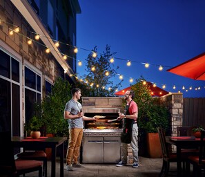 An outdoor patio with a built-in grill, string lights, and red umbrellas. - TownePlace Suites By Marriott Denver Downtown (Denver)