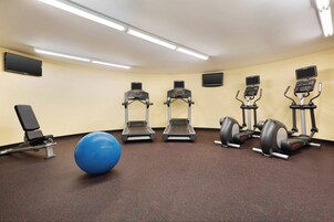 A gym with treadmills, an elliptical, a stationary bike, a blue exercise ball, and a bench.