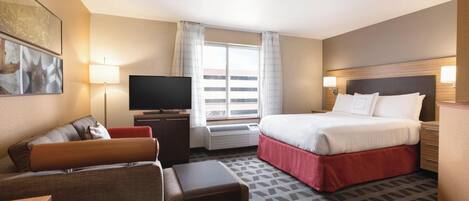 Una habitación de hotel con cama, televisor, sofá, escritorio y ventana con cortinas.