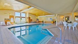 Et indendørs swimmingpool med krystalklart vand, omgivet af hvide stole og borde.