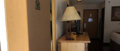 A hallway with a wooden bench, a lamp, and a door with a number sign.