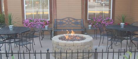 An outdoor seating area with stone fire pit, metal chairs, and tables.