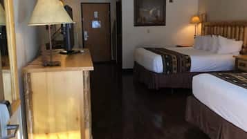 Ein Hotelzimmer mit einem Holztisch, einem Bett mit gemustertem Überwurf, einem Nachttisch mit Lampe und einem Gemälde an der Wand.