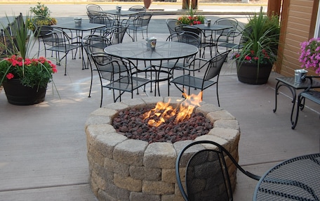 An outdoor seating area with round tables and chairs, a fire pit, and potted plants.