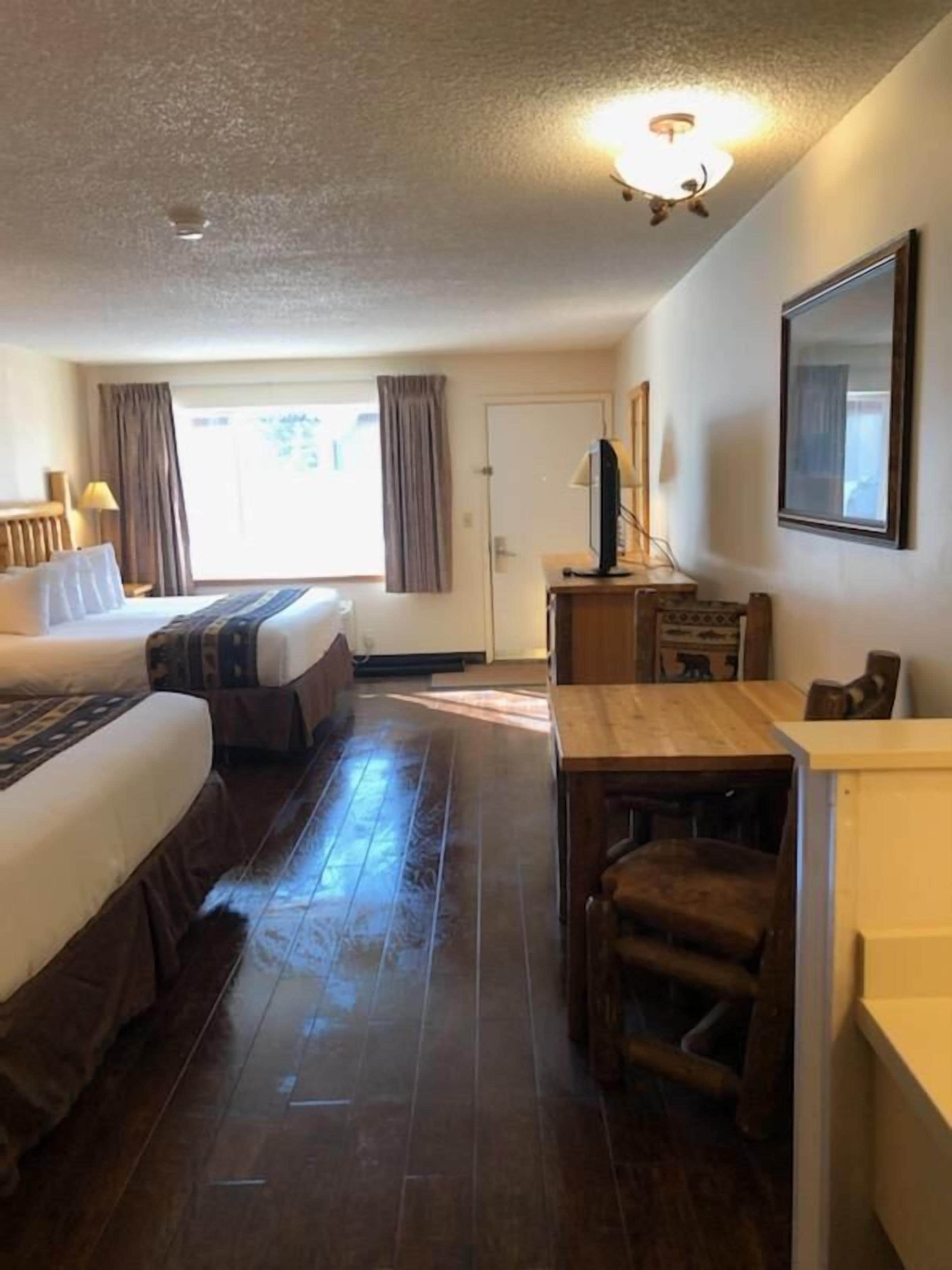 A hotel room with two beds, a desk, a chair, a television, and a door.