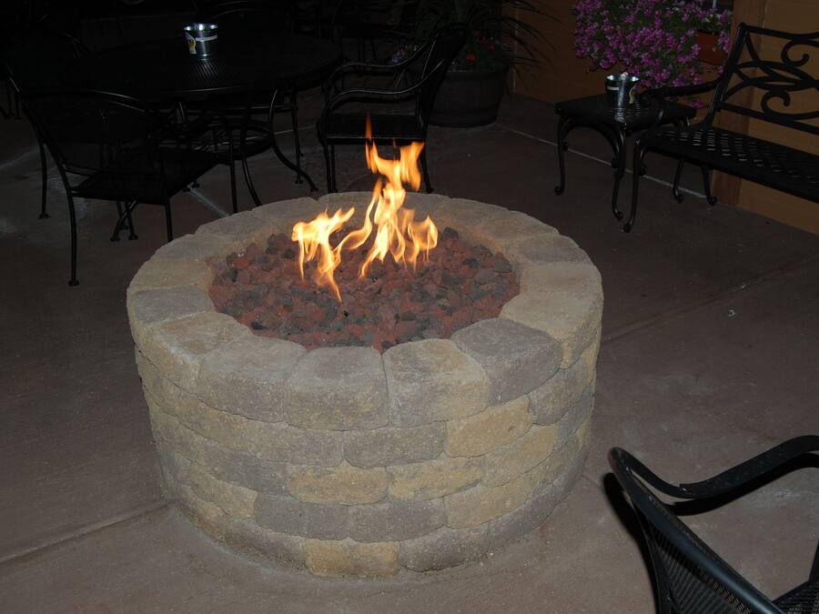 Una chimenea de piedra con llamas, rodeada de mobiliario de exterior.