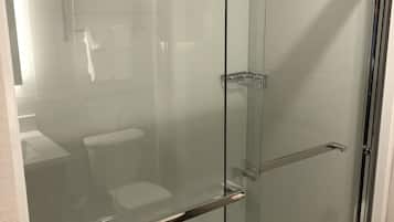 Ducha con cerramiento de vidrio, un grifo cromado y una repisa.
