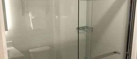 A glass-enclosed shower with a chrome handle and a shelf.