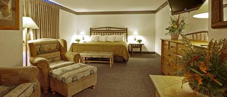 A hotel room with a bed, two armchairs, a wooden dresser, a television, and a desk with a lamp.
