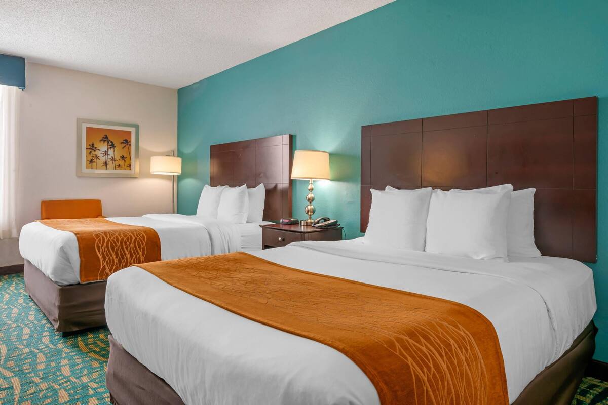 Een hotelkamer met twee bedden, teal muren en een kamerbreed tapijt met een patroon.