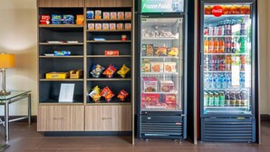 Un distributeur automatique orné d’une affiche « Coca-Cola, très frais », un congélateur avec une étiquette « Produits surgelés », et un présentoir à friandises contenant divers produits alimentaires.