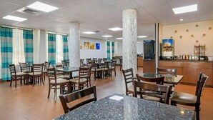 Un grand espace dédié à la salle à manger, avec plusieurs tables et chaises, un comptoir équipé d’un distributeur de boissons et un réfrigérateur.