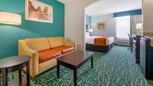 Une chambre d’hôtel avec un canapé à motifs, une petite table, un lit recouvert d’un plaid orange et un bureau.