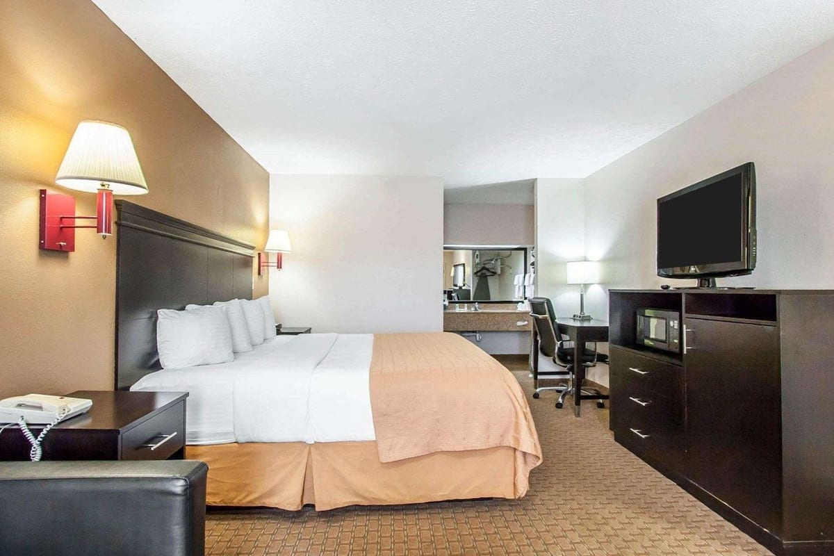 Ein Hotelzimmer mit Bett, Schreibtisch, Stuhl, Fernseher, Telefon und Spiegel.