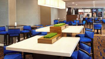 Un hall d’hôtel doté de plusieurs espaces aménagés avec des sièges, notamment des tables et des chaises, ainsi qu’un bar équipé d’un écran de télévision.