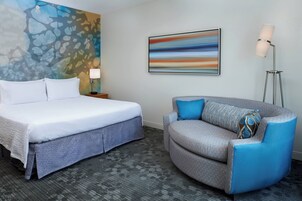 A hotel room with a bed, a sofa, a lamp, and a painting on the wall.