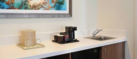 A kitchen area with a coffee maker, cups, and a sink.