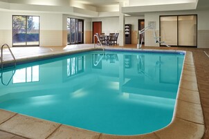 An indoor swimming pool with clear water, a wooden deck surrounding it, and a set of stairs leading into the pool.