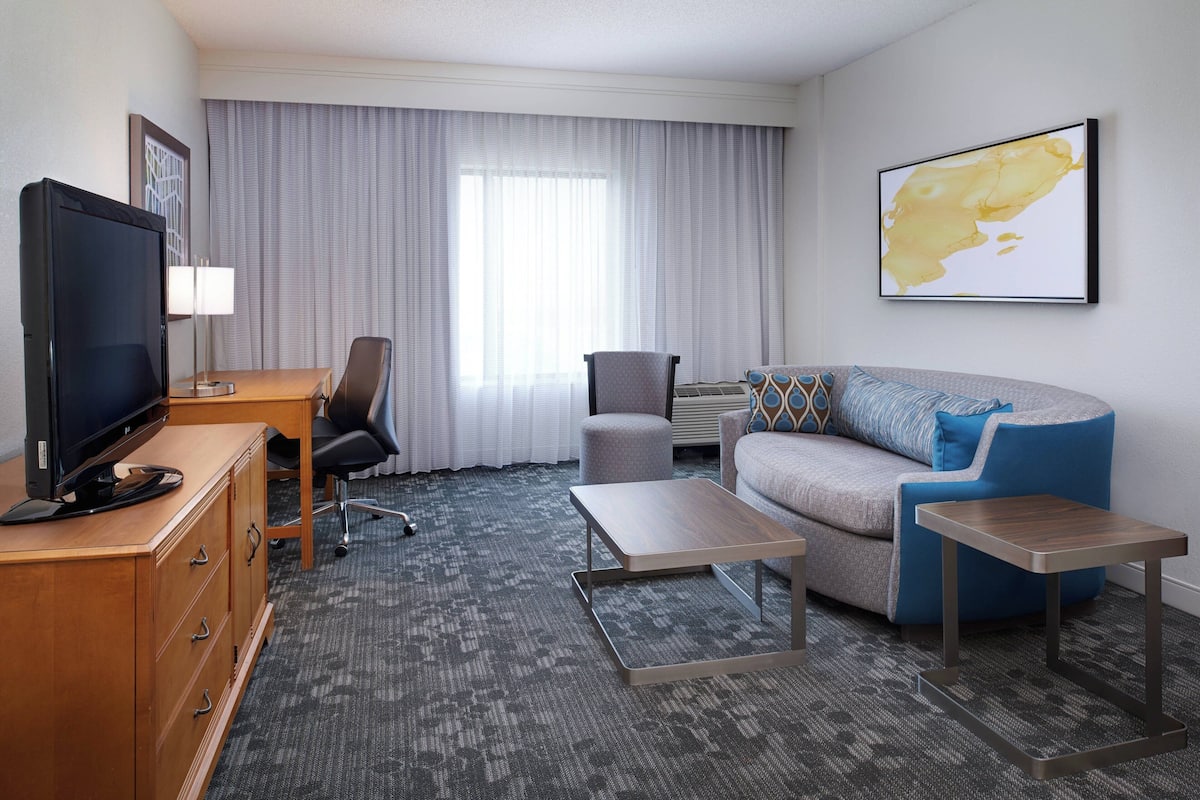 A hotel room with a TV, desk, chair, sofa, and coffee table.