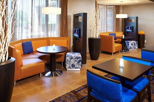 A hotel lobby with a sofa, chairs, a table, a TV, and decorative plants.