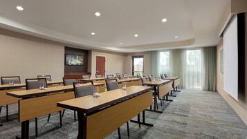 A conference room with multiple tables and chairs, a projector screen, and a large window with curtains.