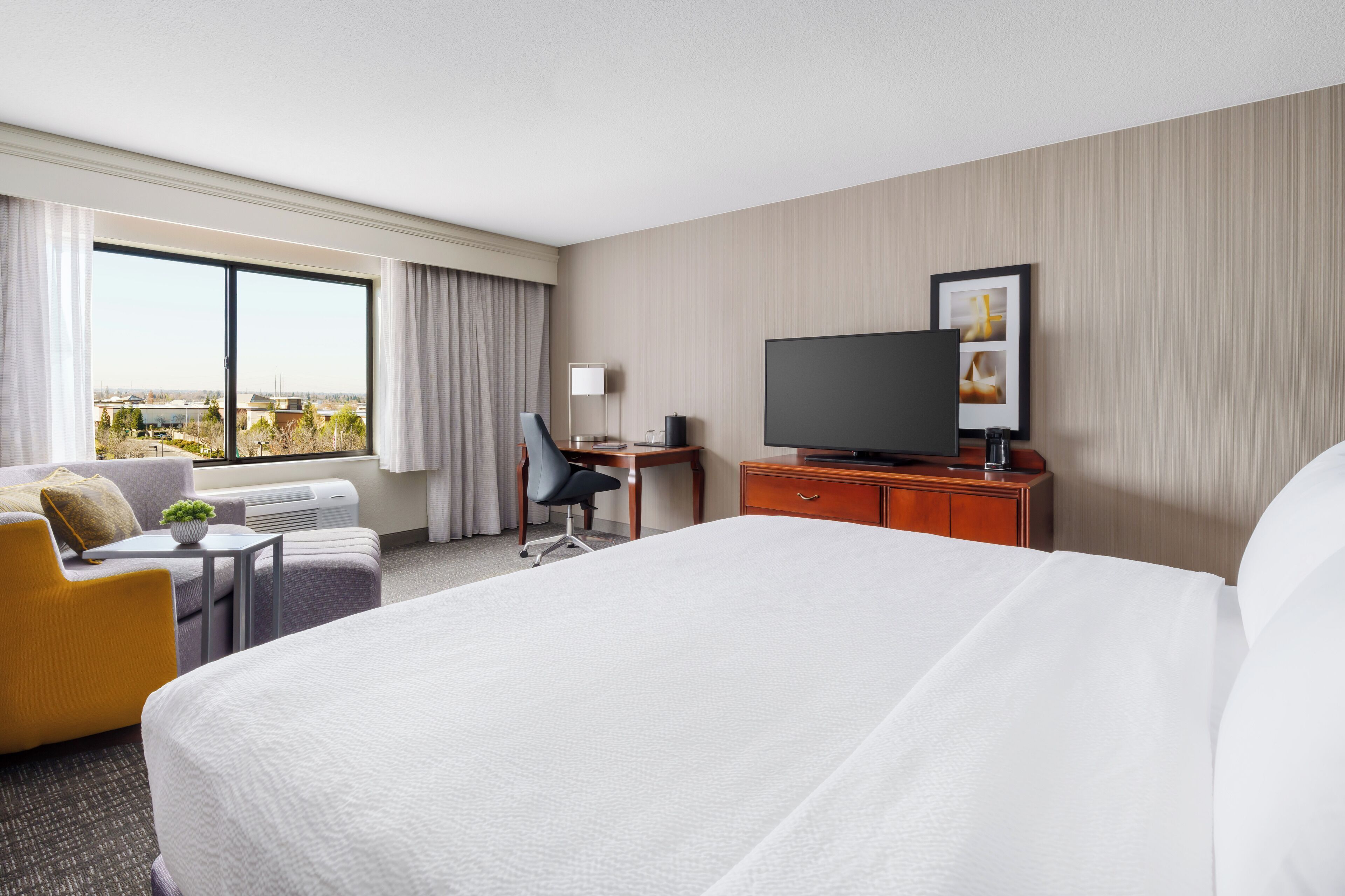 Habitación de hotel con una cama grande, un escritorio, una silla, un televisor y una ventana con vistas.