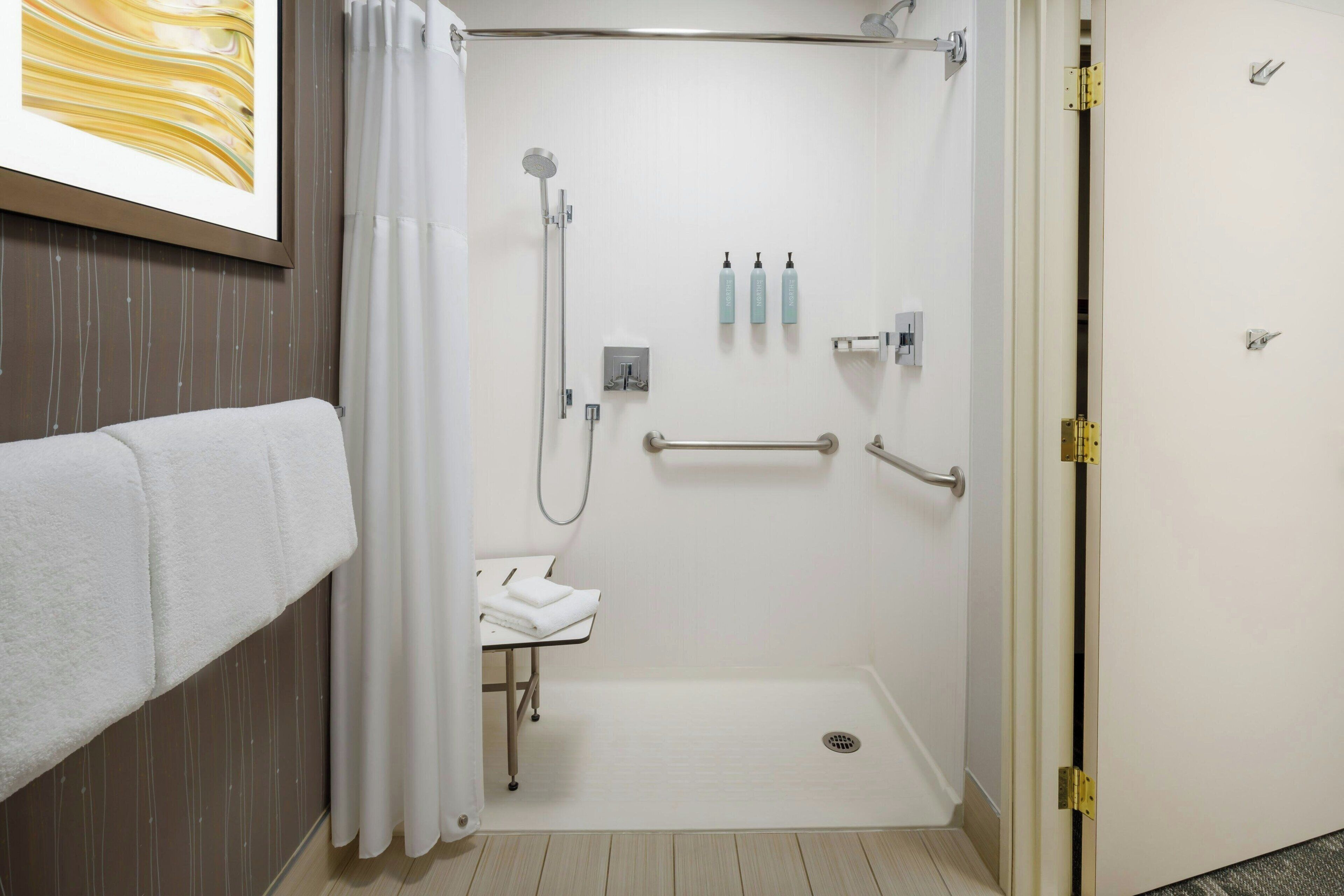 A modern bathroom with a shower, a sink, and a toilet. There are towels on a rack, and toiletries on the wall.