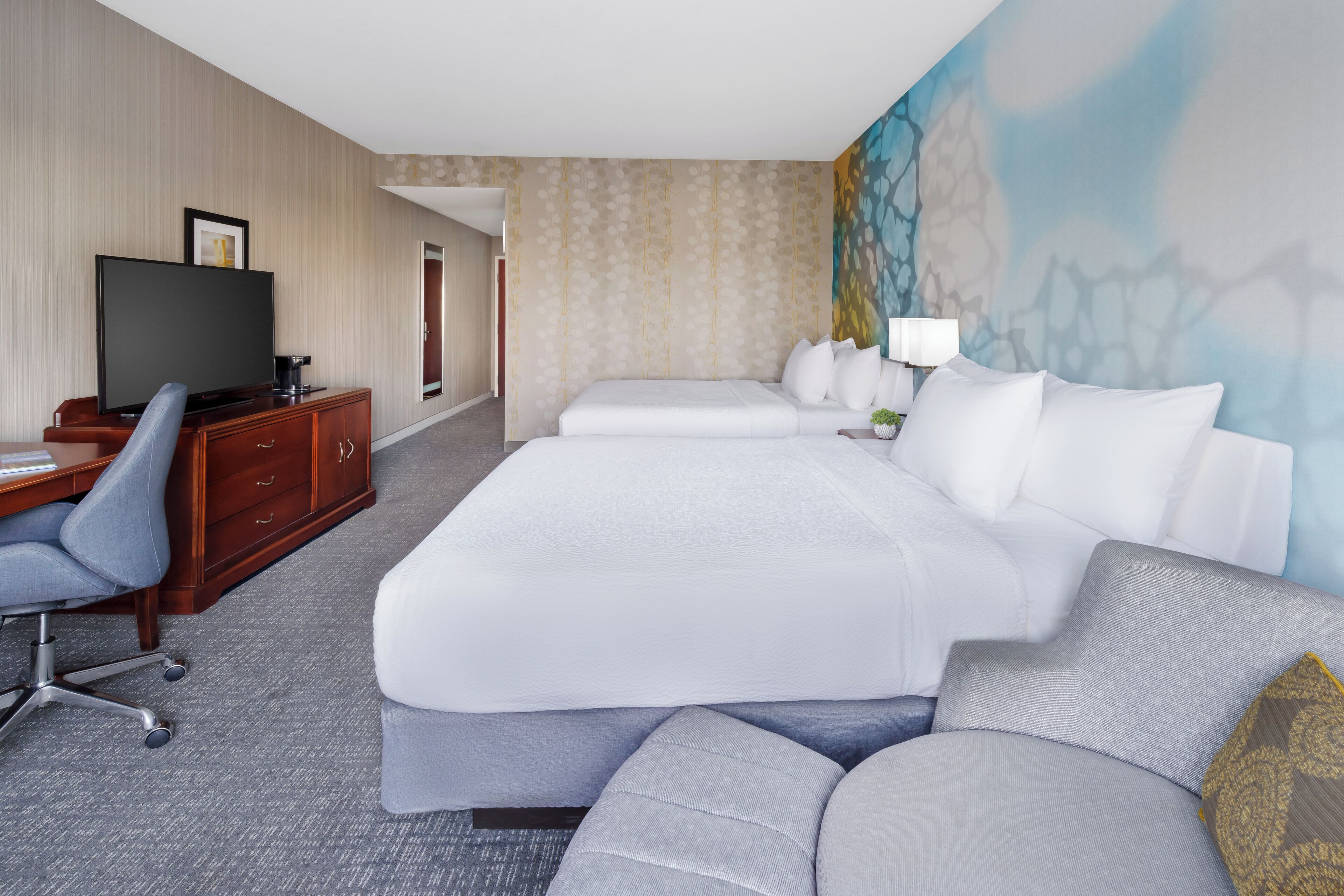 A hotel room with a large bed, a desk with a chair, a television, and a painting on the wall.