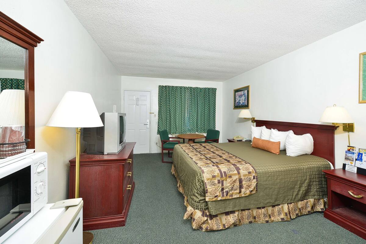 A hotel room with a bed, a desk, a chair, a microwave, and a television.