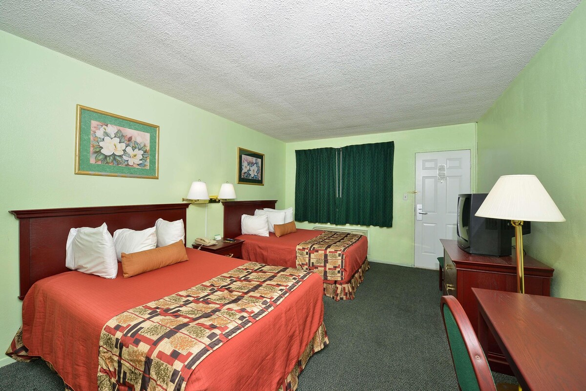A hotel room with two beds, a desk, a TV, and a lamp.