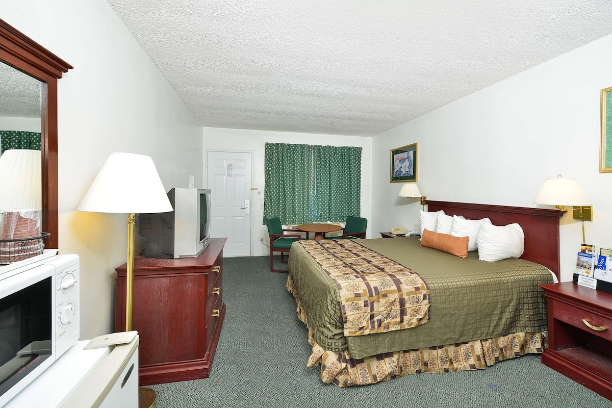 A hotel room with a bed, a desk, a chair, a TV, a microwave, and a door.