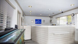Un área de recepción con una vitrina de vidrio, un mostrador de recepción, un cartel que dice 'Americas Best Value Inn' y un reloj en la pared.
