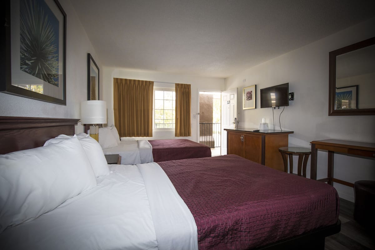 A hotel room with two beds, a desk, a chair, a TV, and a door leading to a balcony.