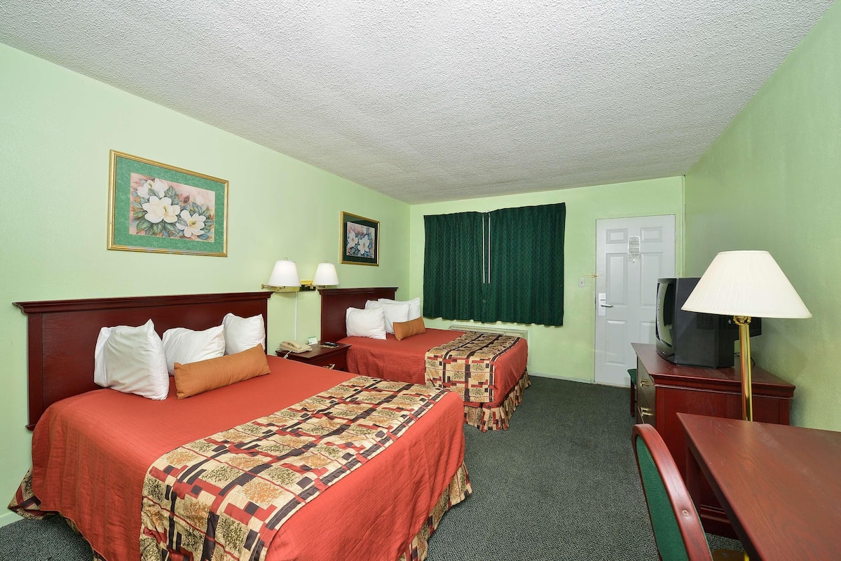 A hotel room with two beds, a desk, a TV, and a lamp.