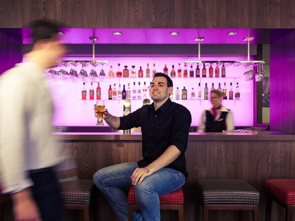 A bar area with a bartender, a seated customer, and a blurred person walking by.