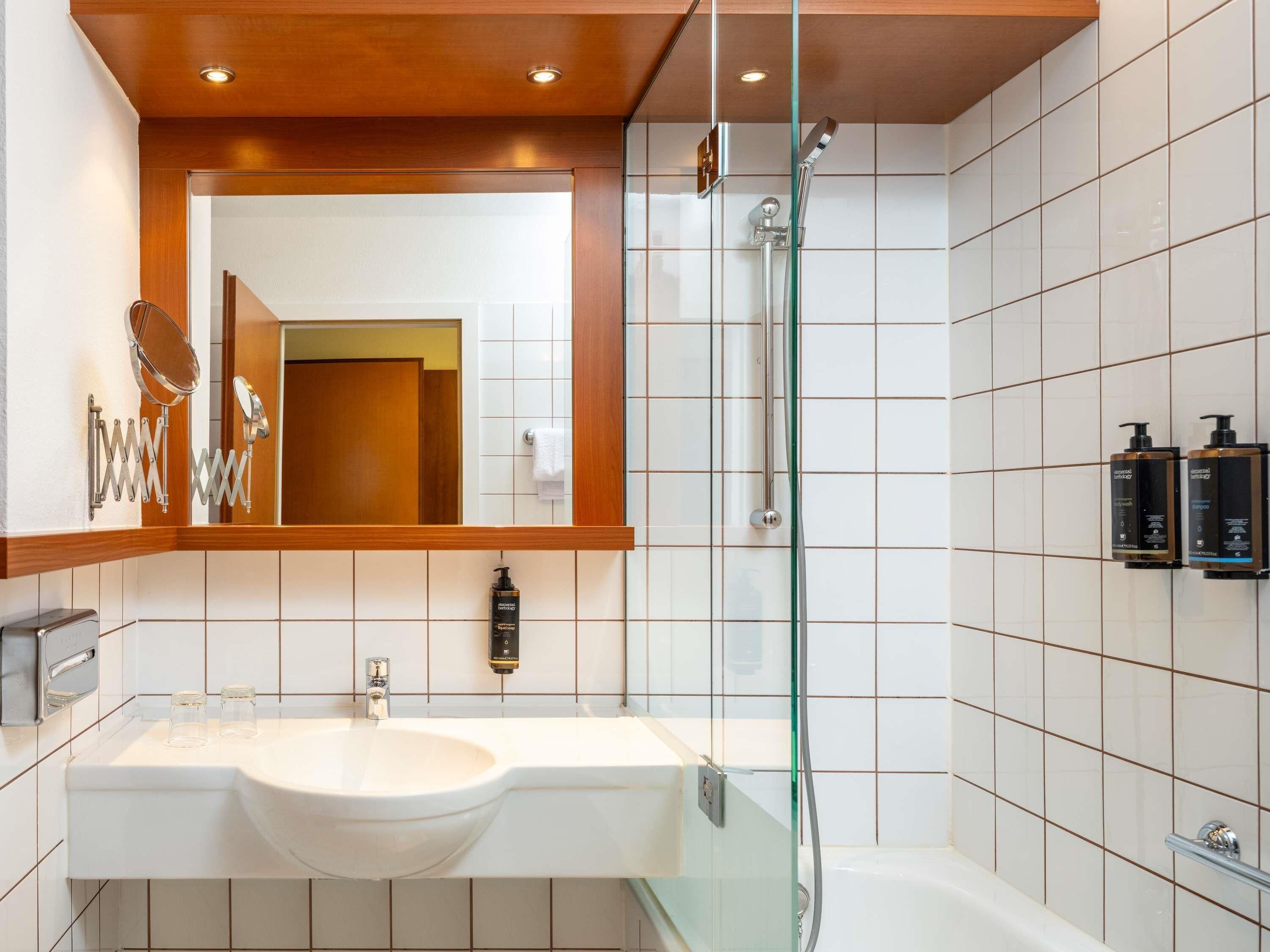 Un baño moderno con ducha envuelta en vidrio, un lavabo blanco y un espejo grande.