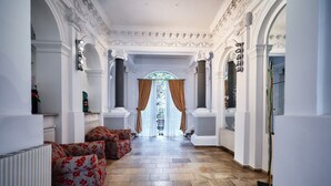 Un pasillo con un sofá floral, columnas blancas y vistas a través de una ventana con cortinas.
