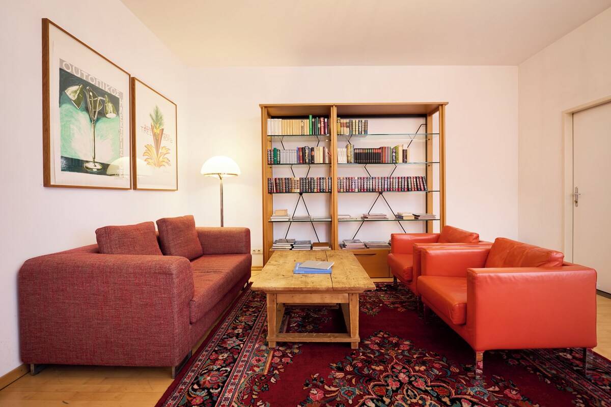 A living room with a red sofa, a wooden coffee table, and a bookshelf filled with books.