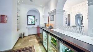 Zona de bar con mostrador, vasos y un refrigerador lleno de botellas.