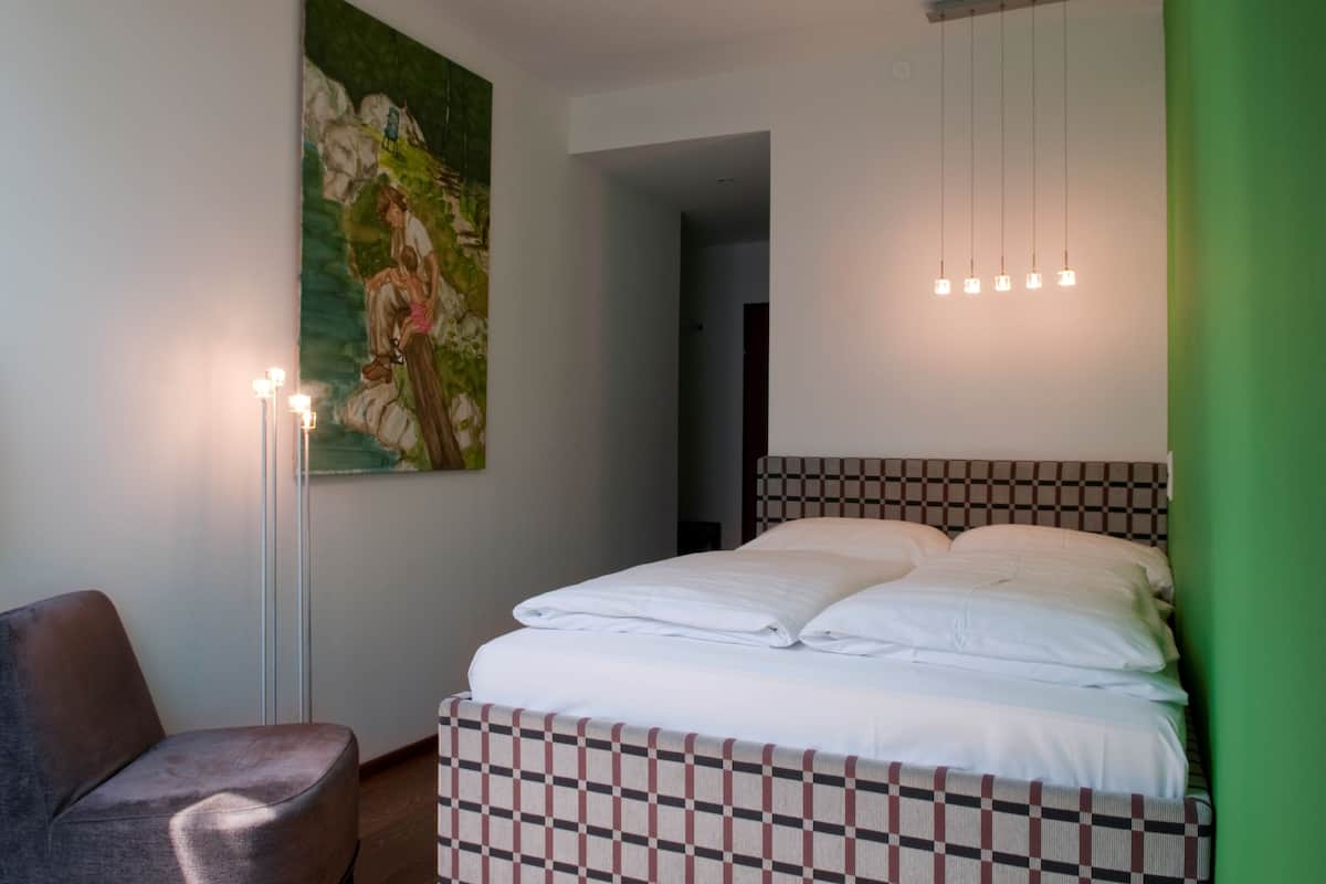 A bedroom with a checkered headboard, a large painting on the wall, and a bedside table with a lamp.