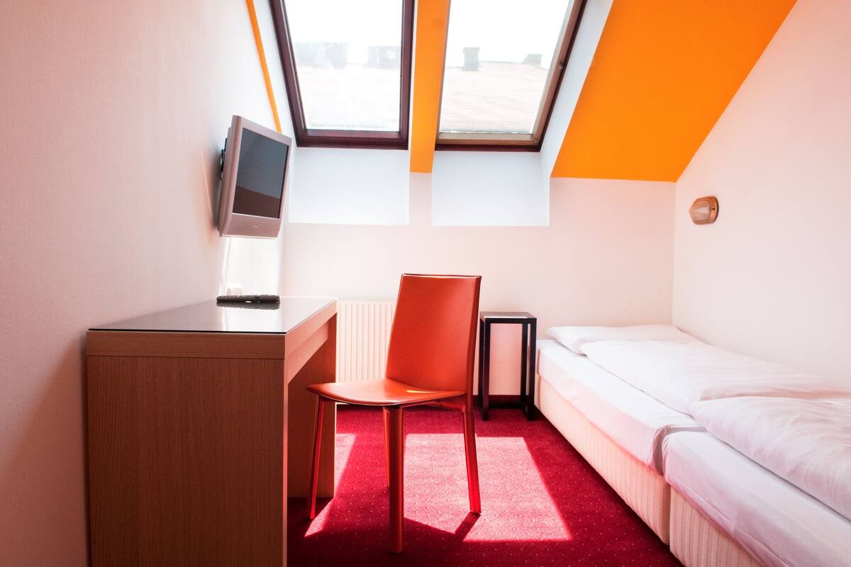 A room with a desk, chair, bed, and a skylight.